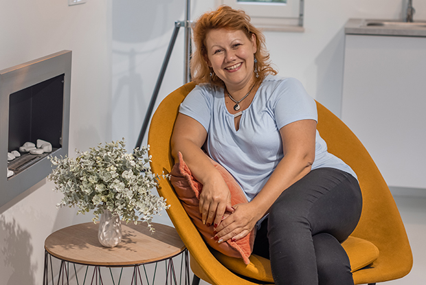 Natural Pharmaceuticals VitaSolaris® D3 Középkorú nő fekete hajjal és kockás ingben, virágos kert háttérrel.